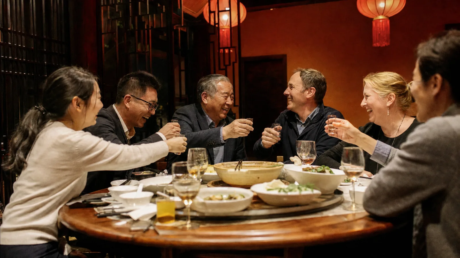 A company boss raises a glass with his Western guests and his team around a round table at a celebration dinner