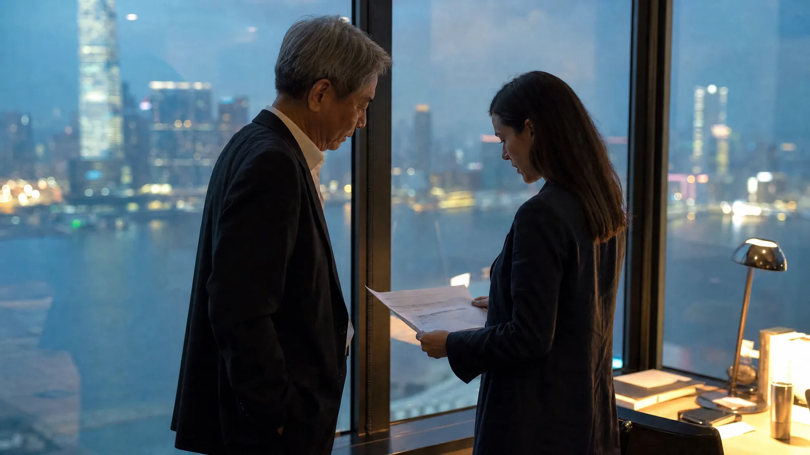 A company chairman and a Western consultant read a document at a Hong Kong office window at dusk, Victoria Harbour lit behind them